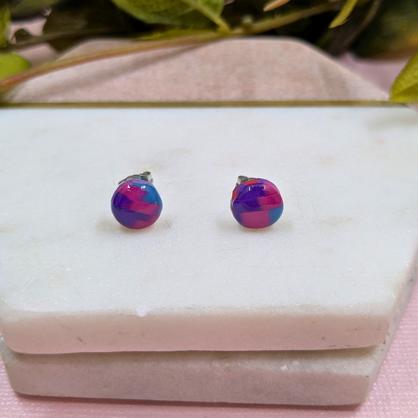 Multicolored round earrings on a white stone surface with green leaves in the background