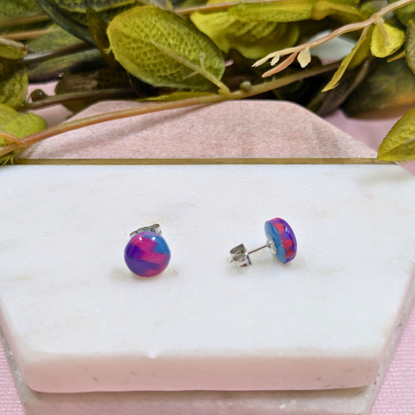 Multicoloured round earrings on a white marble slab with green leaves in the background