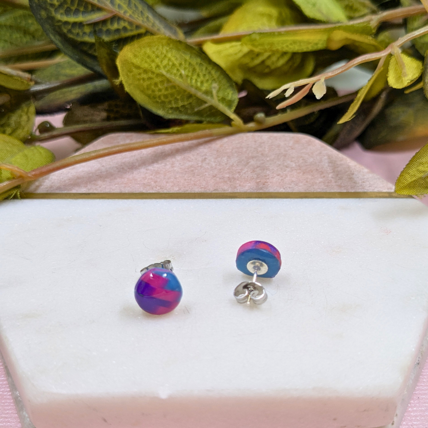 Multicolored round earrings on a white surface with green leaves in the background