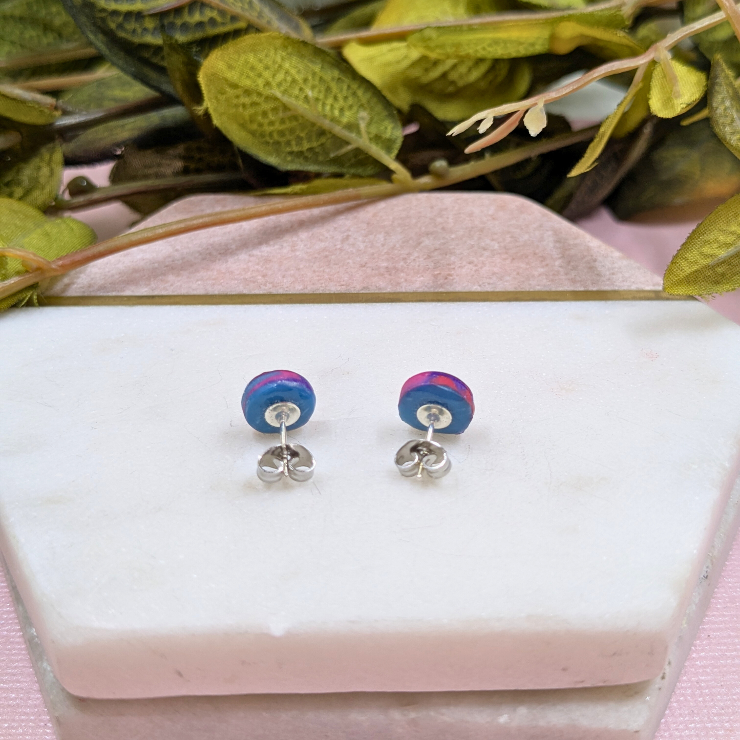 Colourful round earrings on a white stand with green leaves in the background