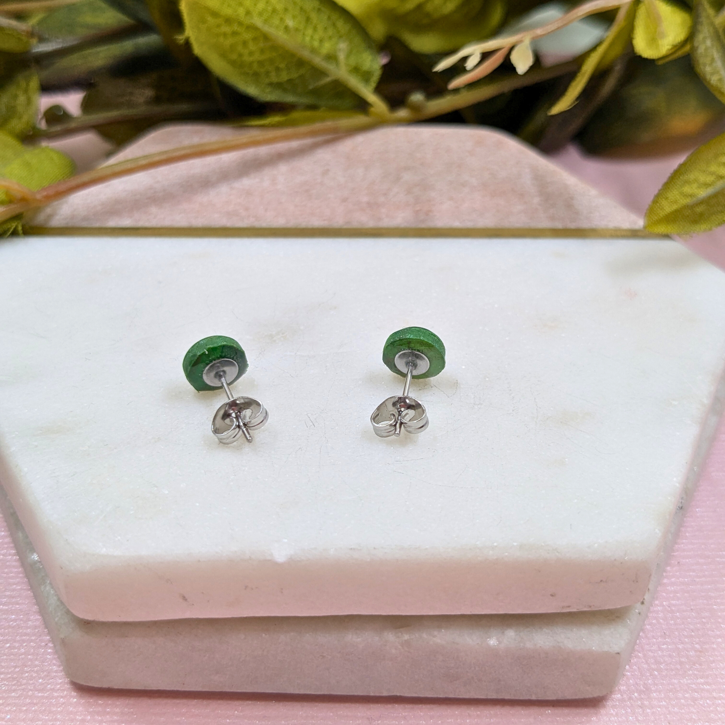 Green earrings on a white jewelry display with a pink background