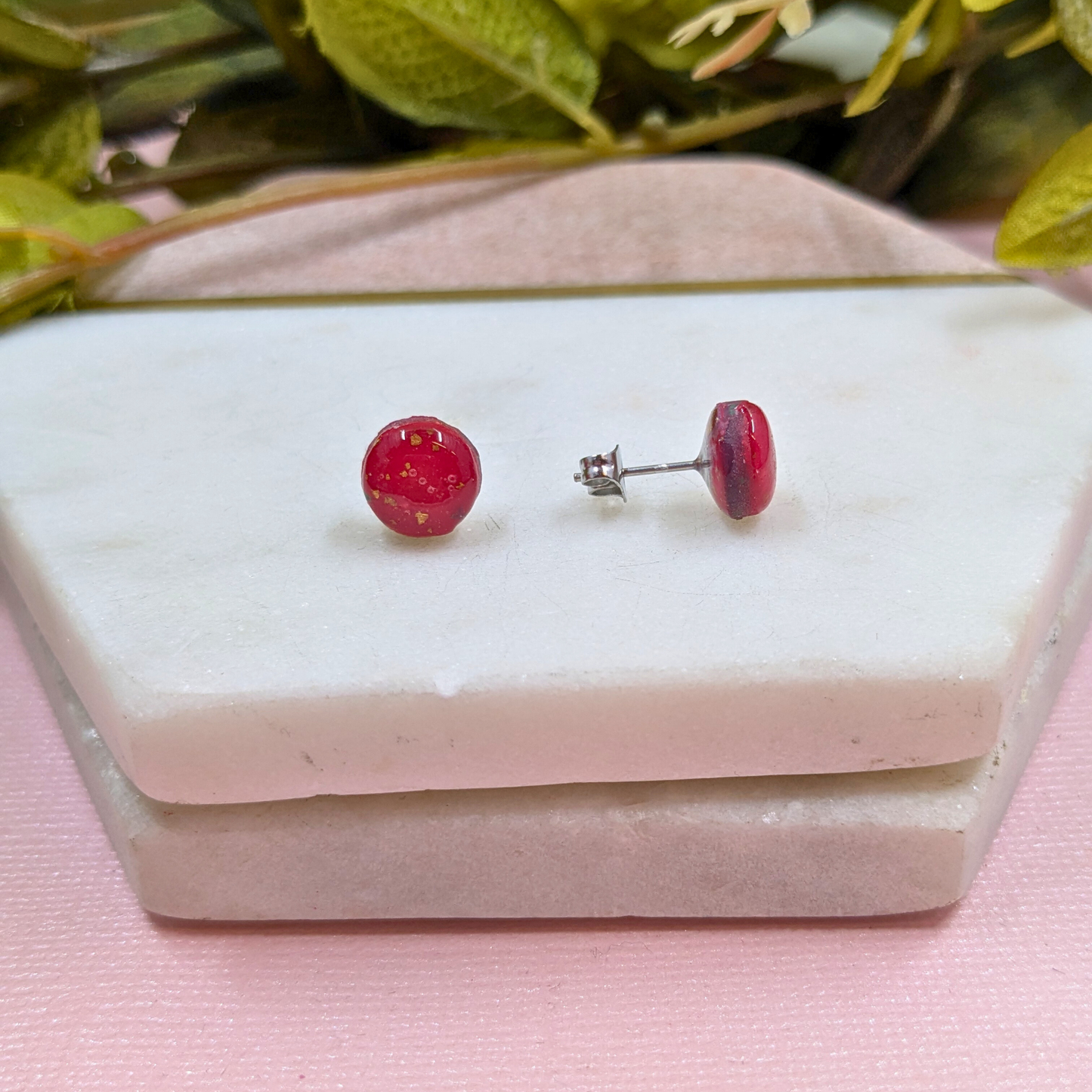 Red round earrings on a white stone surface with a pink background