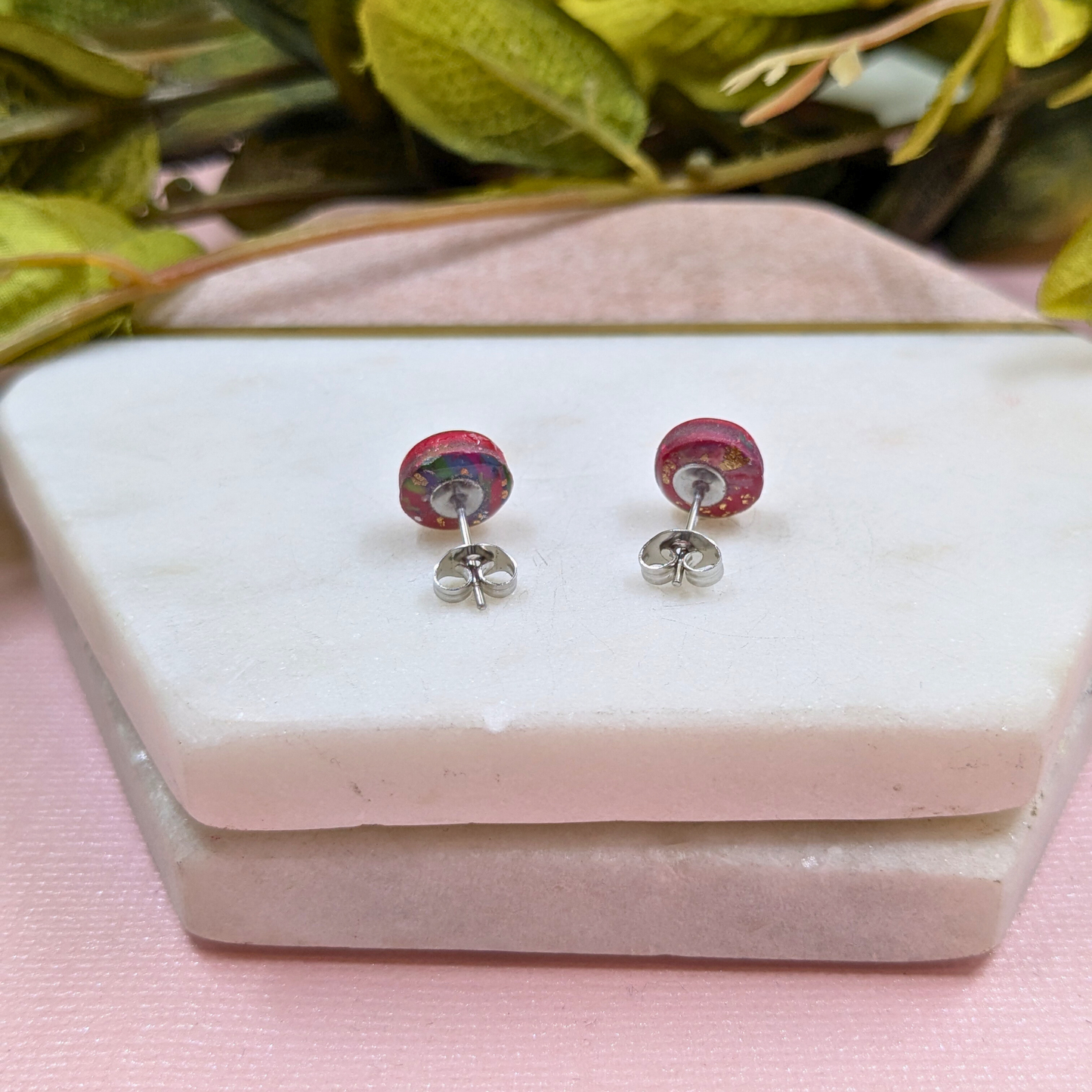 Pair of pink and silver earrings on a white stone surface with green leaves in the background.