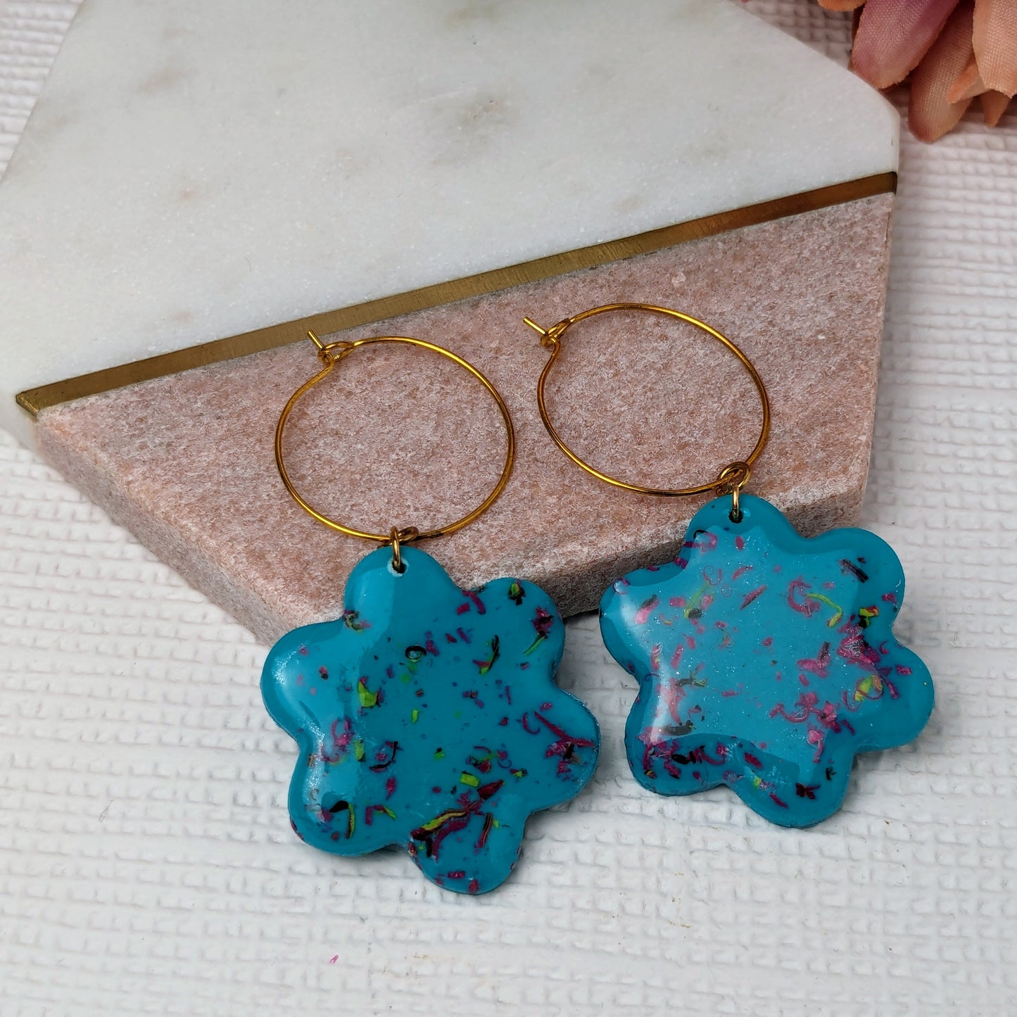 A pair of large, blue polymer clay flower earrings with gold plated hooks, displayed on a beige surface.