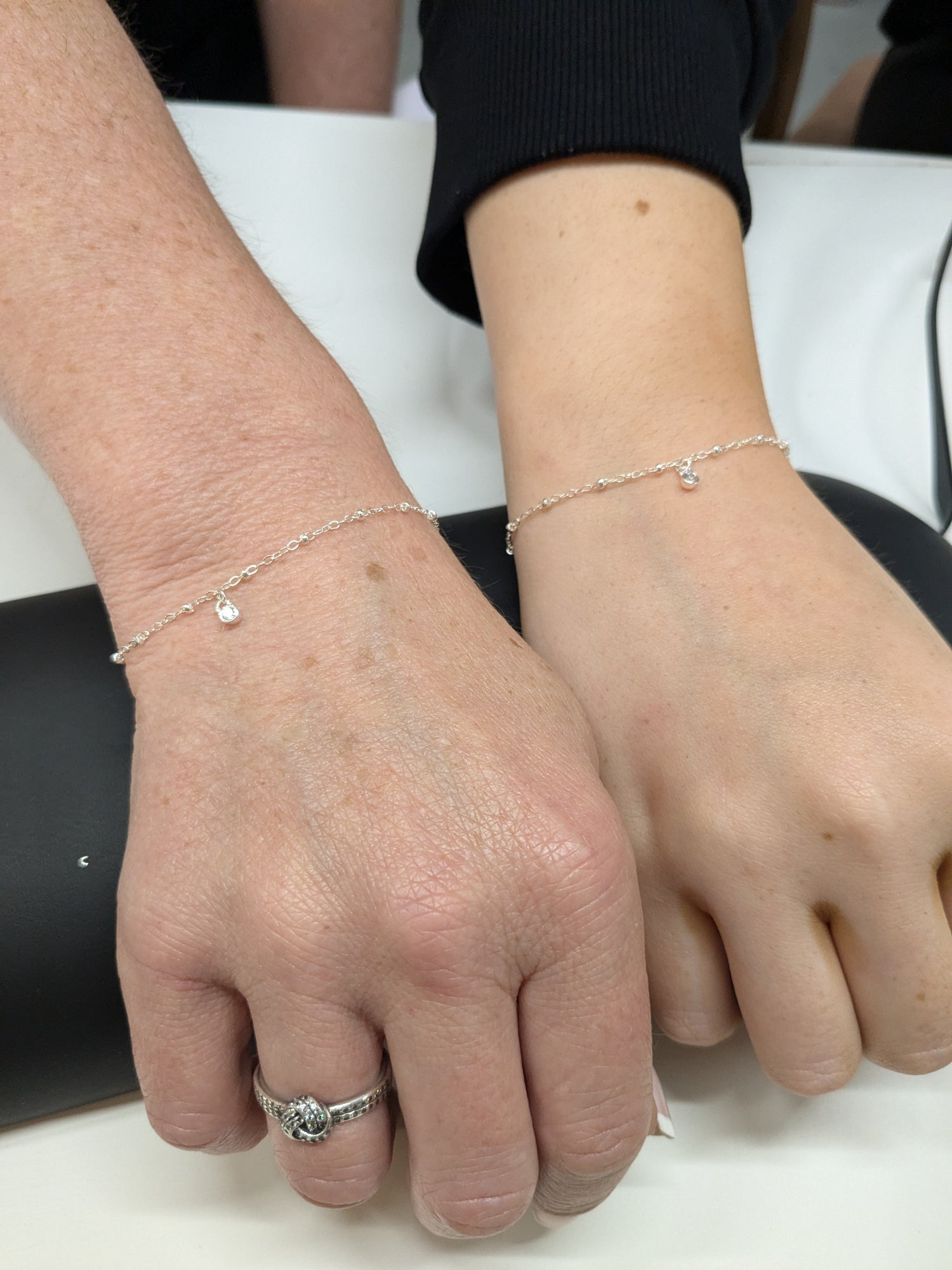 Mother and daughter bonds. Photo shows 2 women's wrists featuring matching permanent welded sterling silver bracelets with crystal charms dangling from them. These bracelets have been created by Welded Bonds Permanent Jewellery by Created By Lau.