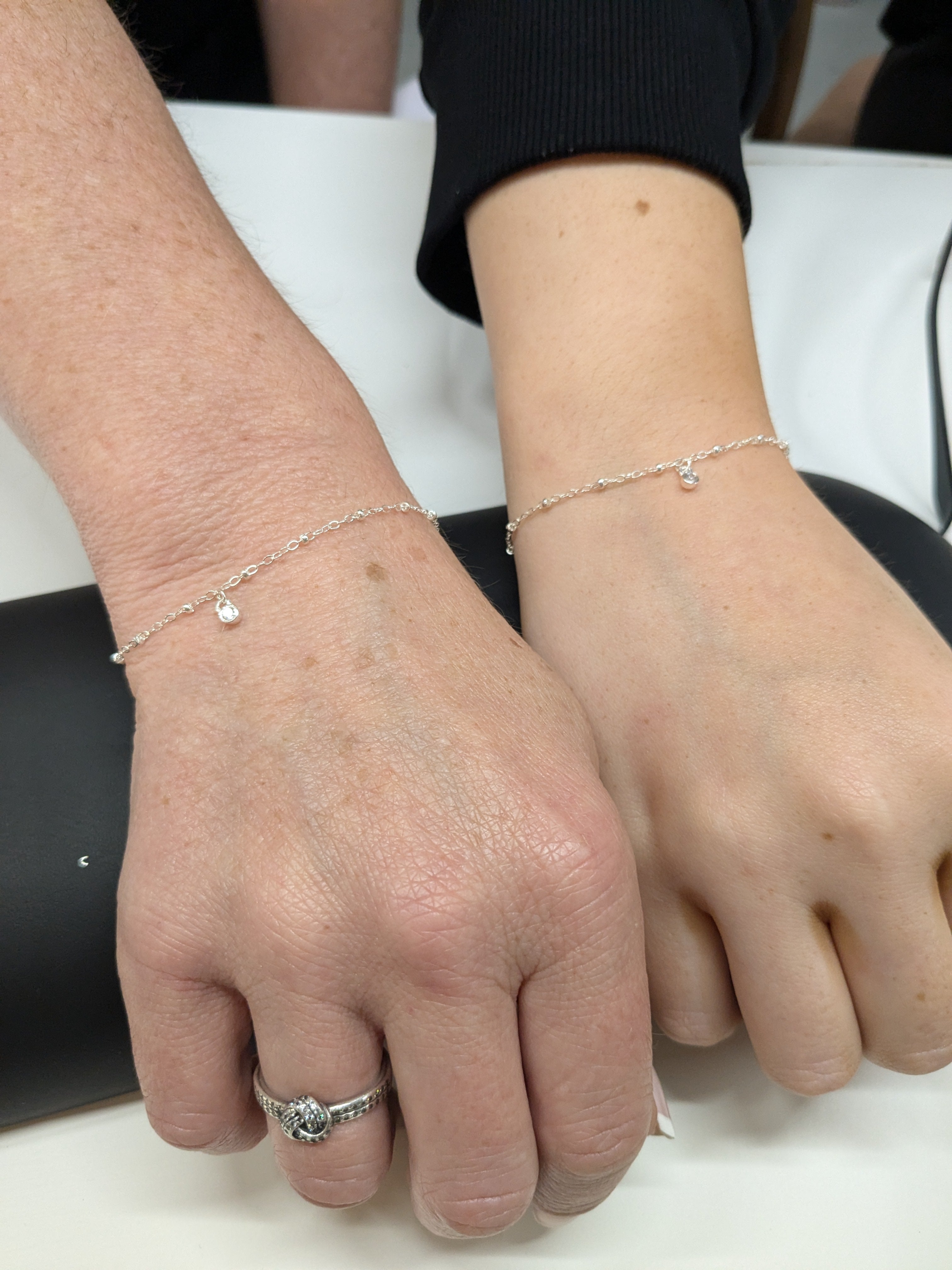 Mother and daughter bonds. Photo shows 2 women's wrists featuring matching permanent welded sterling silver bracelets with crystal charms dangling from them. These bracelets have been created by Welded Bonds Permanent Jewellery by Created By Lau.