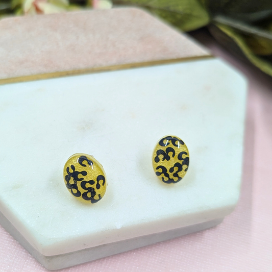Close up of handmade oval resin stud earrings showing black animal print glitter on yellow resin background