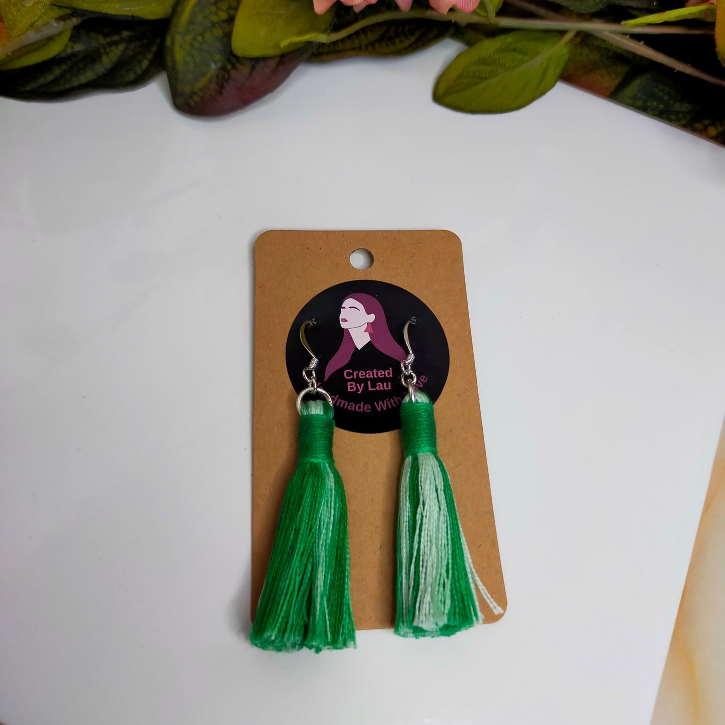 Green tassel earrings on a branded card with flowers in the background