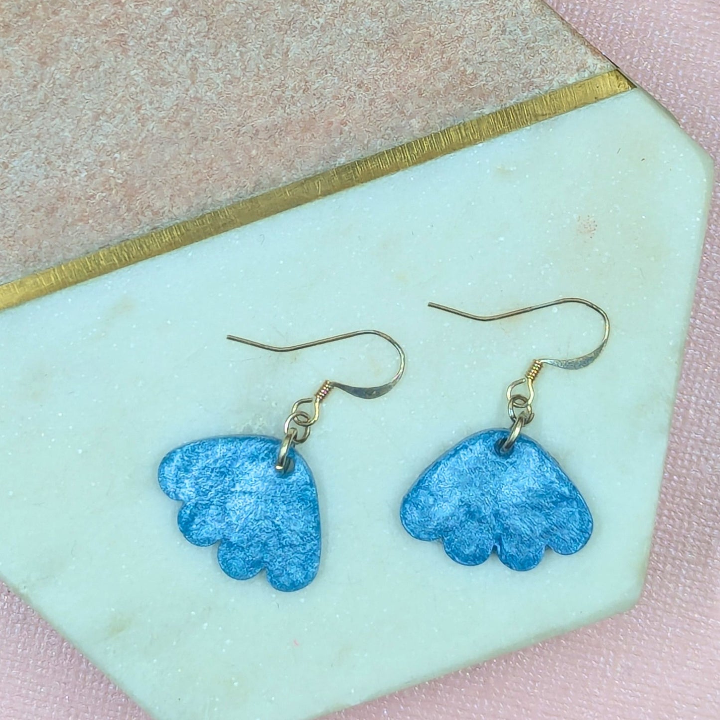 Blue flower-shaped earrings on a light green card with pink border