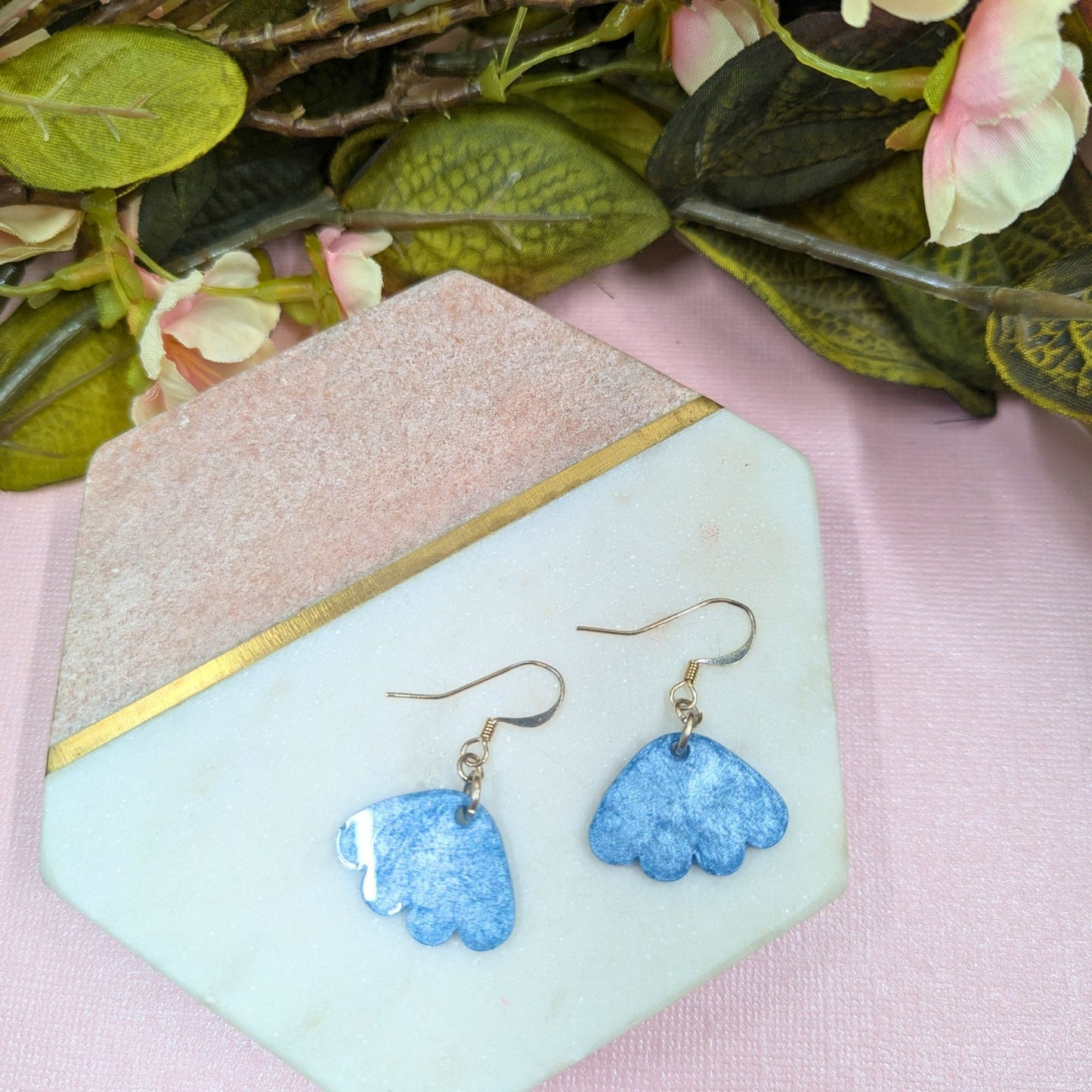 Blue flower-shaped earrings on a light green stand with floral background