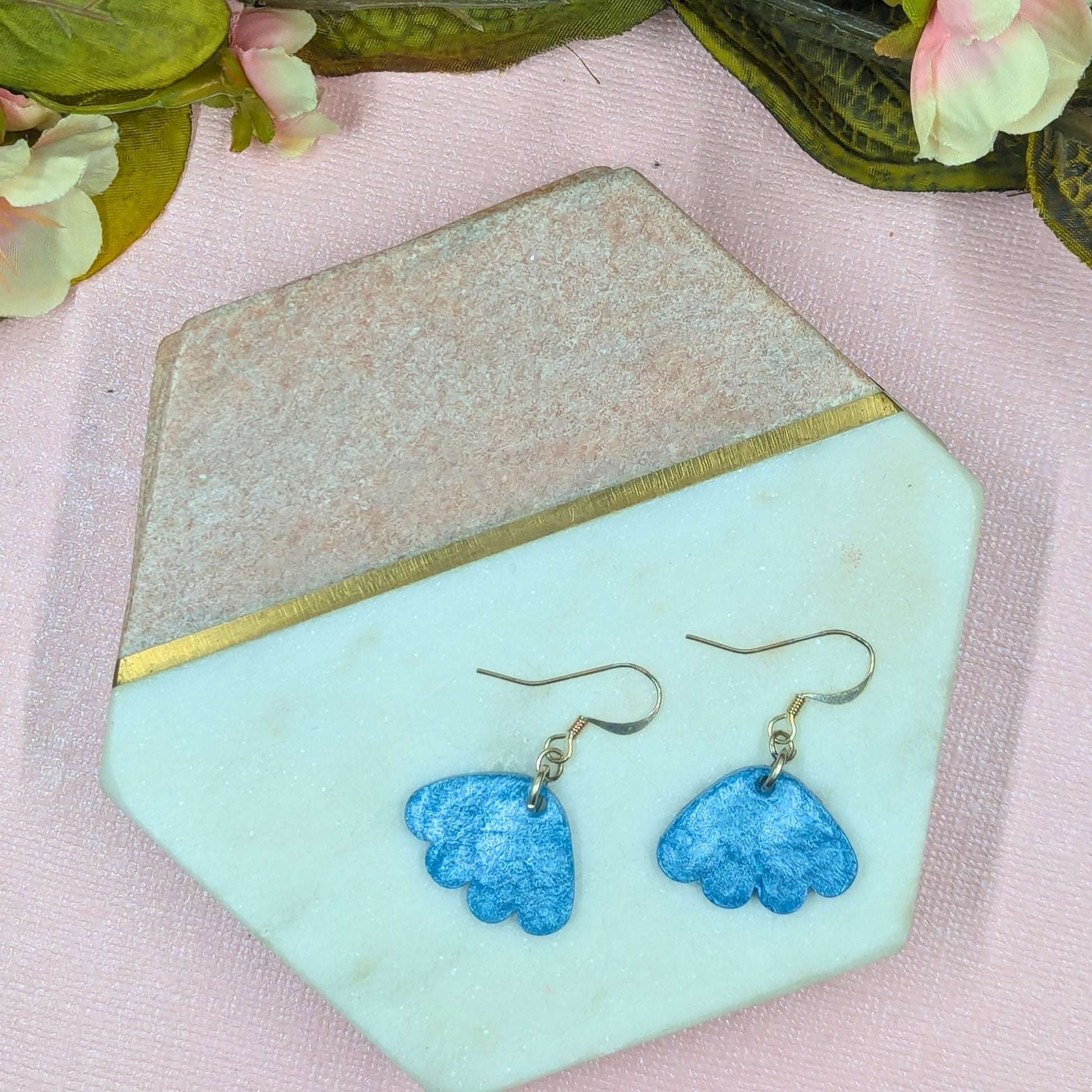 Blue flower earrings on a light green stand with flowers in the background