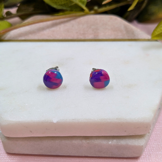 Multicolored round earrings on a white stone surface with green leaves in the background