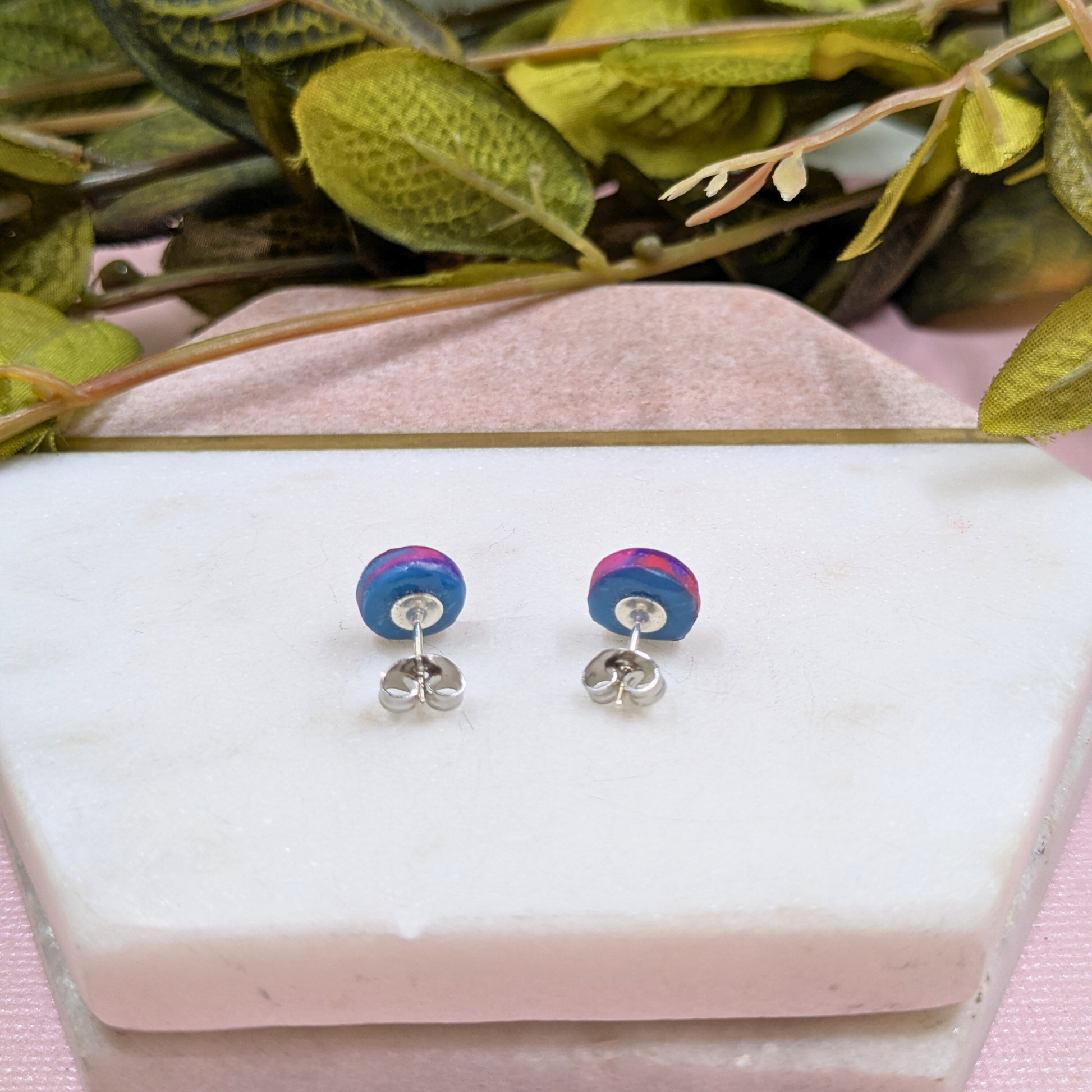 Colourful round earrings on a white stand with green leaves in the background