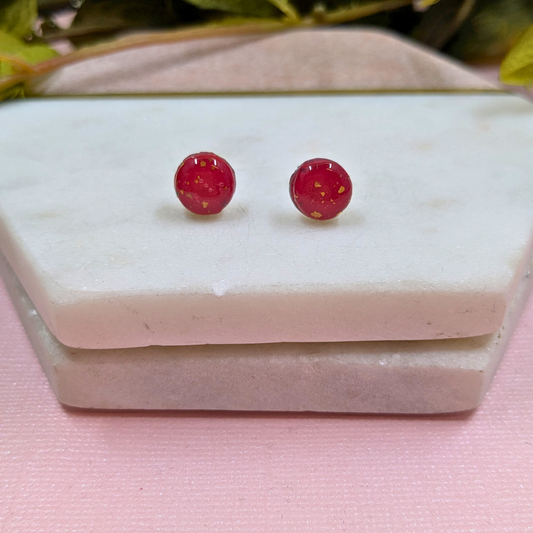Red round earrings on a white marble surface with a pink fabric background