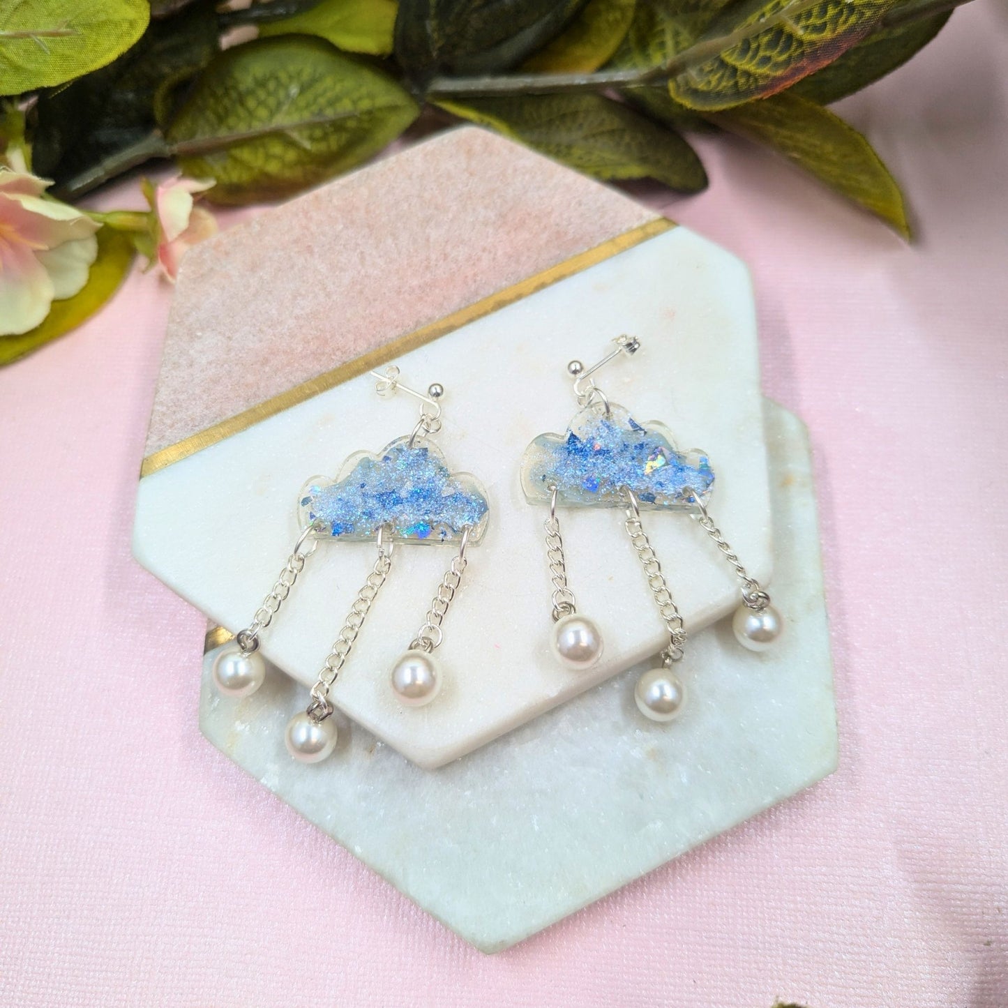 Pair of earrings with blue cloud and pearl designs on a decorative stone surface.