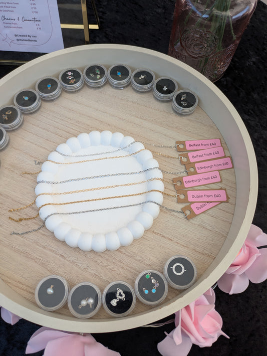 Wooden circular organiser with Premium Permanent Jewellery and decorative elements on a dark surface.