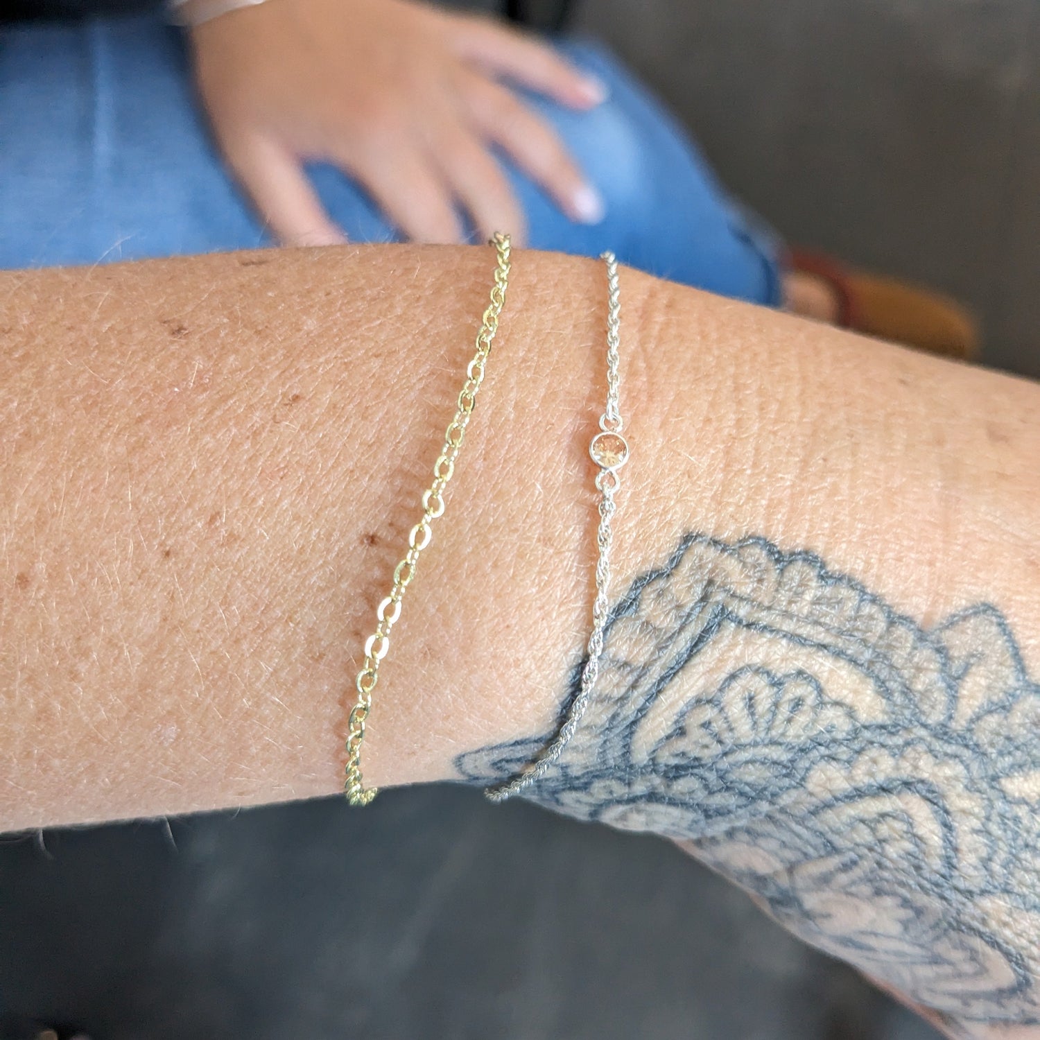 Gold chain bracelet on a person's wrist with a tattoo, blurred background